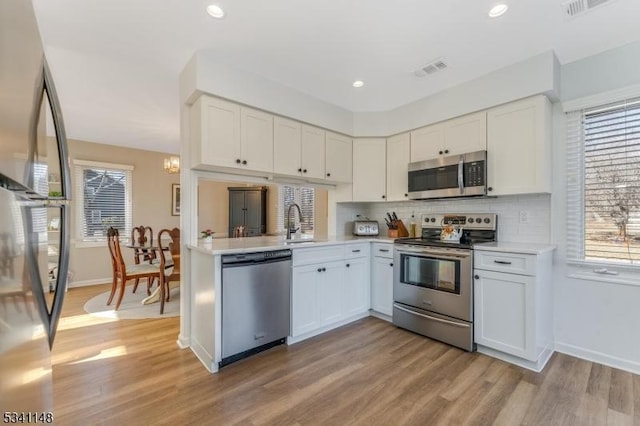 kitchen with appliances with stainless steel finishes, light wood-type flooring, light countertops, baseboards, and white cabinets