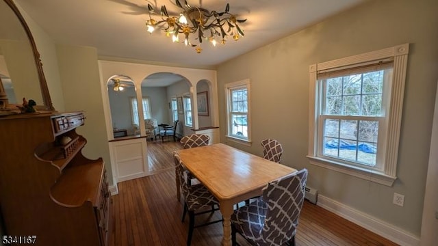 dining space with an inviting chandelier, wood finished floors, arched walkways, and baseboards