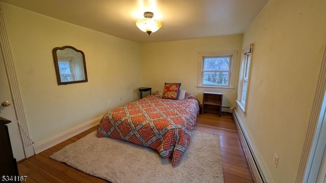 bedroom featuring baseboard heating, a baseboard heating unit, baseboards, and wood finished floors