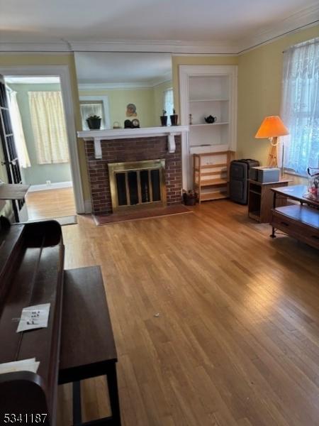 living area featuring built in features, a brick fireplace, crown molding, and wood finished floors