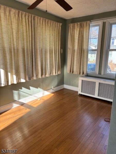 unfurnished room featuring a textured ceiling, dark wood finished floors, radiator heating unit, baseboards, and ceiling fan