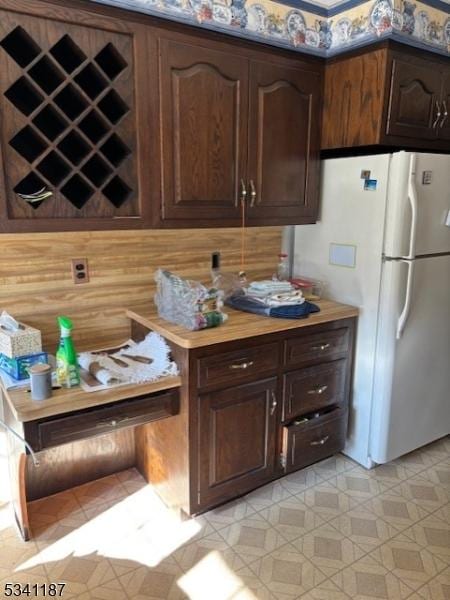 kitchen with dark brown cabinetry, light countertops, and freestanding refrigerator