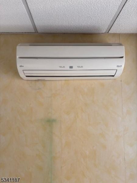 details featuring a wall mounted air conditioner and a drop ceiling