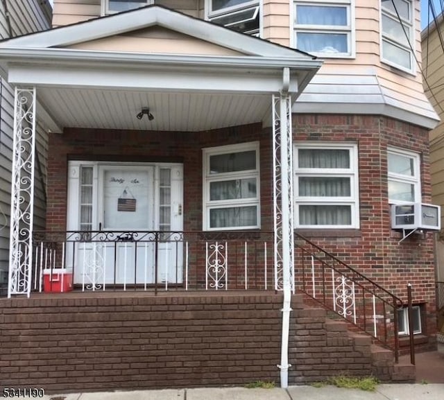 entrance to property featuring a porch, brick siding, and cooling unit