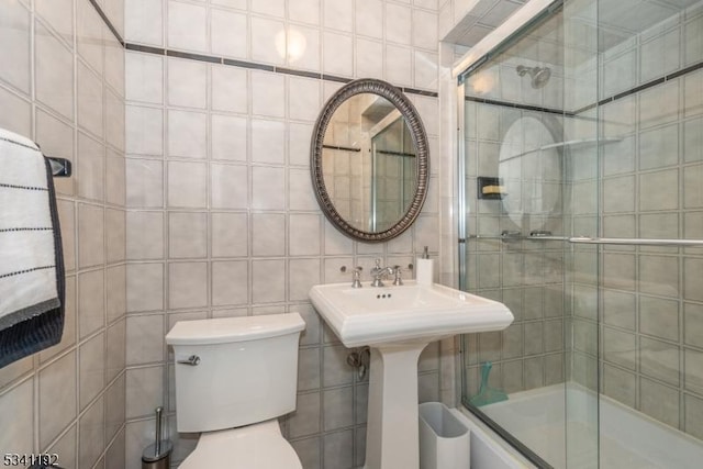 bathroom featuring toilet, a tile shower, and tile walls