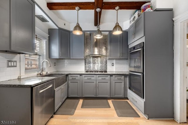 kitchen featuring gray cabinetry, beamed ceiling, dark stone countertops, stainless steel appliances, and wall chimney exhaust hood