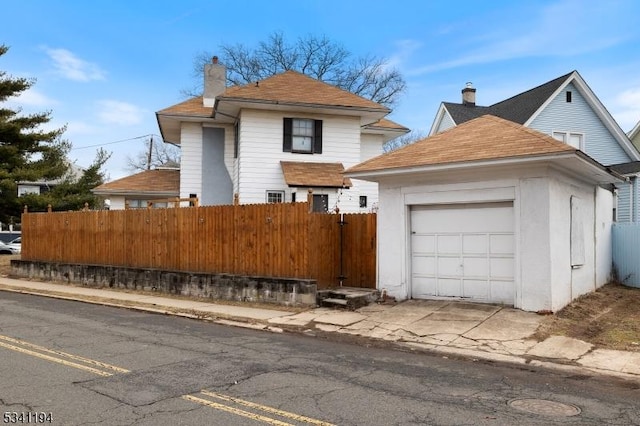 view of front of property featuring an outdoor structure, fence, a detached garage, and a chimney