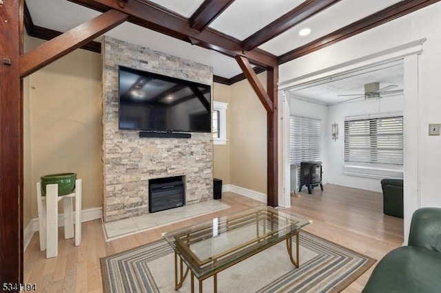 living room with beam ceiling, a stone fireplace, a ceiling fan, and wood finished floors