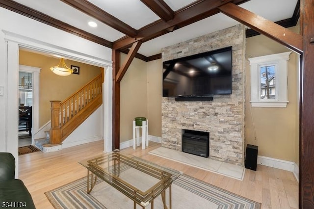 living area with beam ceiling, wood finished floors, a stone fireplace, baseboards, and stairs