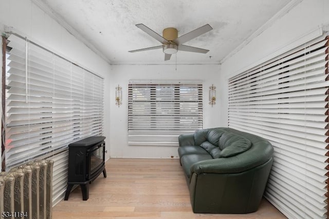 living area with light wood-style flooring, a ceiling fan, a textured ceiling, crown molding, and a wood stove