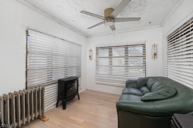 living area featuring a wood stove, radiator, a ceiling fan, and ornamental molding