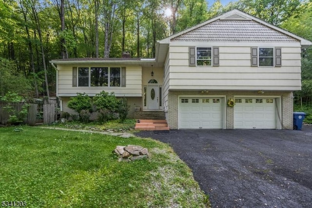 split level home featuring aphalt driveway, a front yard, brick siding, and an attached garage