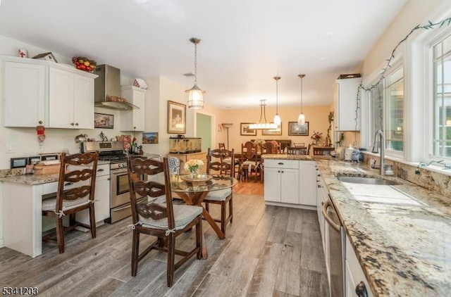 kitchen featuring white cabinets, light wood-style floors, appliances with stainless steel finishes, wall chimney range hood, and a sink