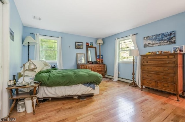 bedroom featuring light wood finished floors, a baseboard radiator, and visible vents