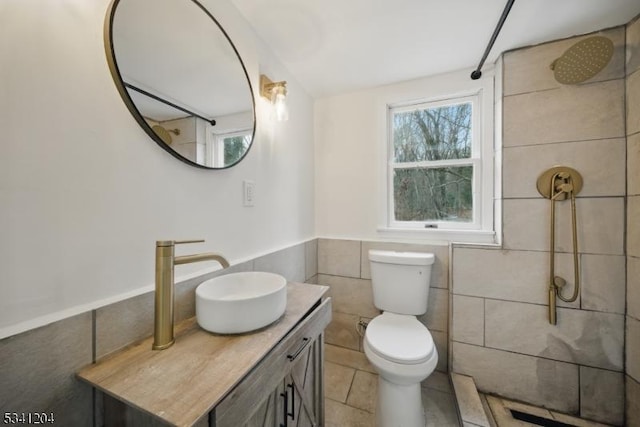 bathroom with tile patterned flooring, toilet, vanity, tile walls, and tiled shower