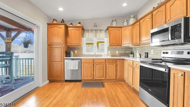 kitchen with tasteful backsplash, stainless steel appliances, light countertops, light wood-style floors, and a sink