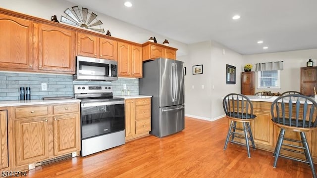 kitchen with light wood finished floors, a breakfast bar area, stainless steel appliances, light countertops, and backsplash