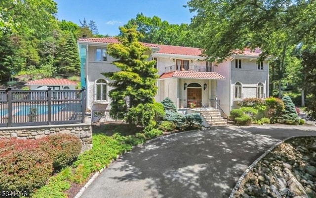 mediterranean / spanish house with a fenced in pool, a tile roof, stucco siding, fence, and a balcony