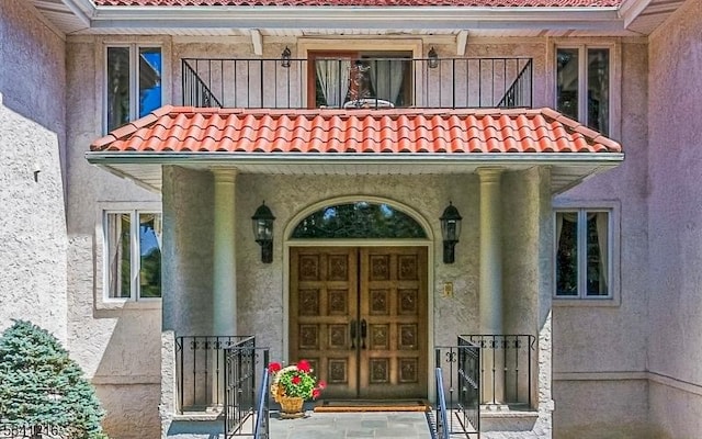 doorway to property with a balcony, a tiled roof, and stucco siding