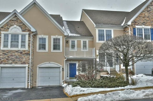 view of property with driveway, a garage, a balcony, stone siding, and stucco siding