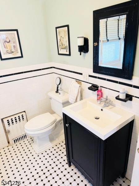 half bath featuring tile walls, vanity, toilet, and radiator