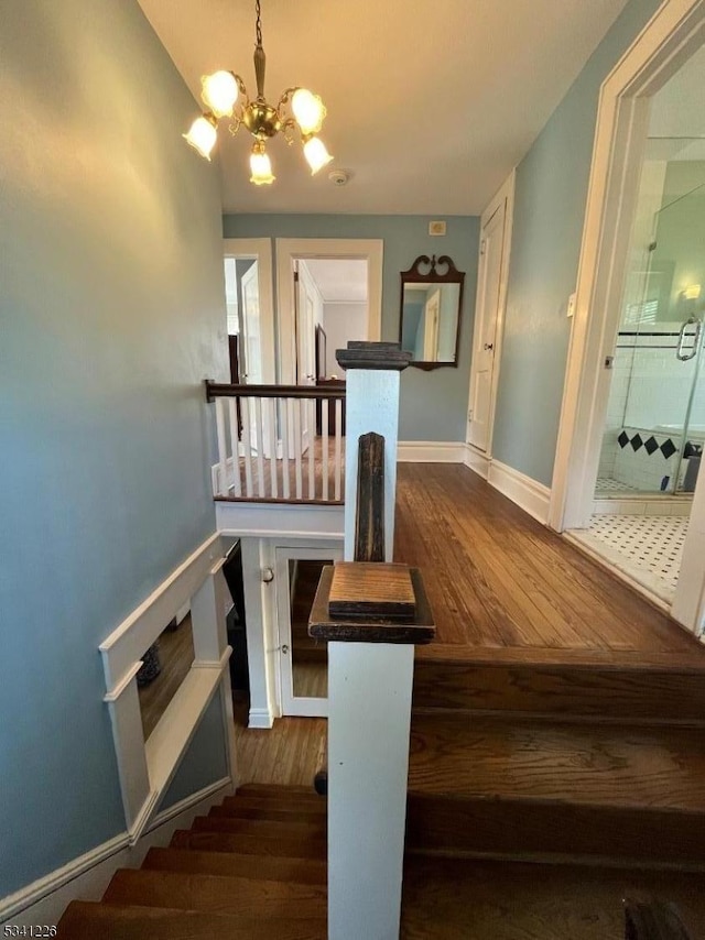 stairway with baseboards, a chandelier, and wood finished floors