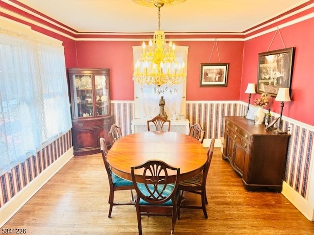 dining space featuring an inviting chandelier, wallpapered walls, ornamental molding, and wood finished floors