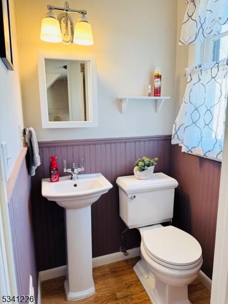 half bath featuring toilet, a wainscoted wall, a sink, and wood finished floors