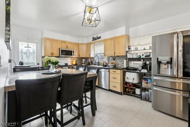 kitchen featuring light brown cabinets, stainless steel appliances, a sink, tasteful backsplash, and dark countertops