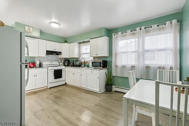 kitchen featuring white appliances, baseboard heating, white cabinets, and under cabinet range hood