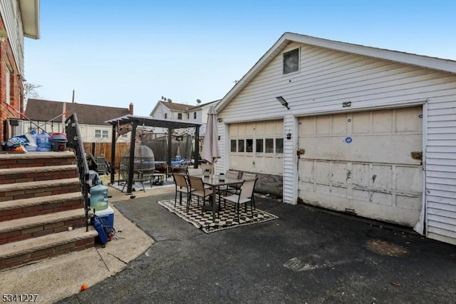 view of patio / terrace featuring a garage, outdoor dining area, fence, and an outdoor structure