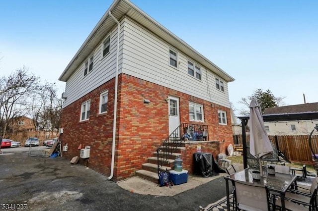 rear view of house featuring brick siding, fence, and a patio