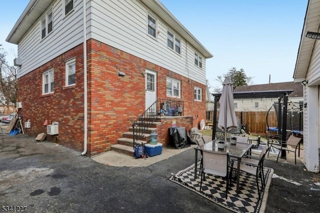 exterior space featuring brick siding, a trampoline, fence, and a patio