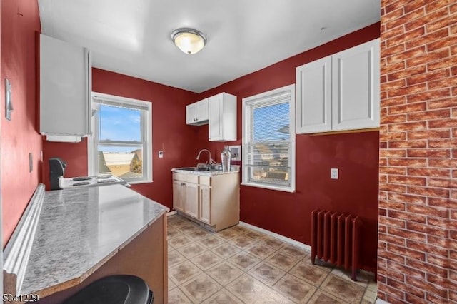 kitchen featuring baseboards, a sink, white cabinetry, and radiator