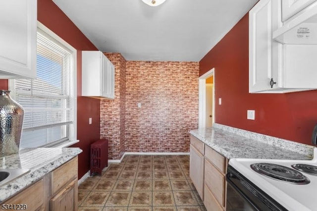 kitchen with electric range oven, an accent wall, white cabinetry, brick wall, and under cabinet range hood