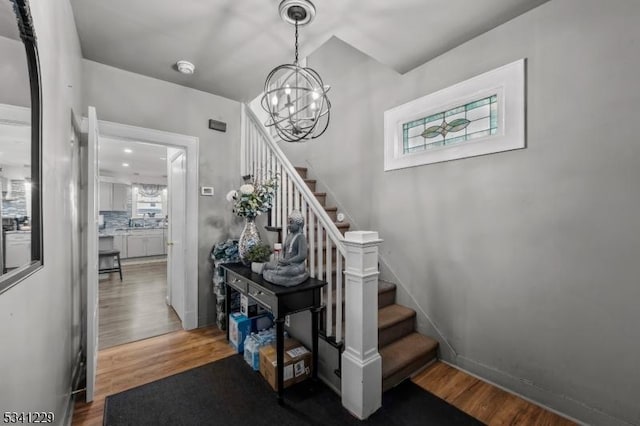 staircase with a chandelier, plenty of natural light, baseboards, and wood finished floors