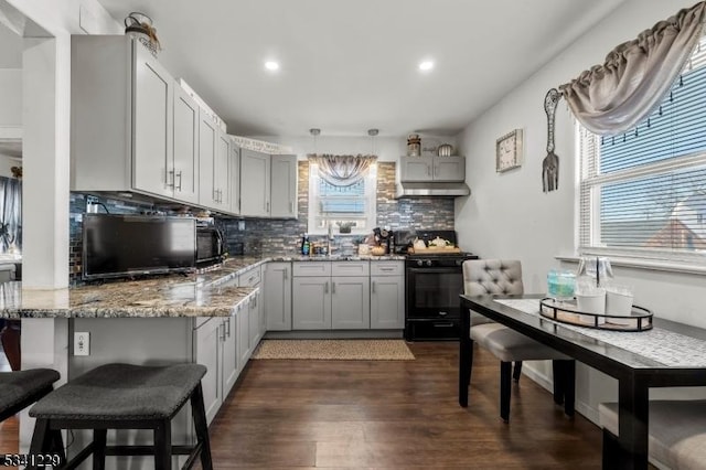 kitchen featuring light stone counters, under cabinet range hood, a sink, black range with gas stovetop, and decorative backsplash