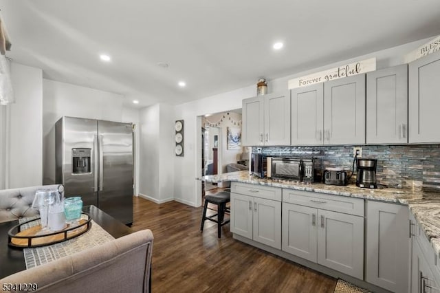 kitchen with black microwave, dark wood finished floors, stainless steel refrigerator with ice dispenser, and decorative backsplash