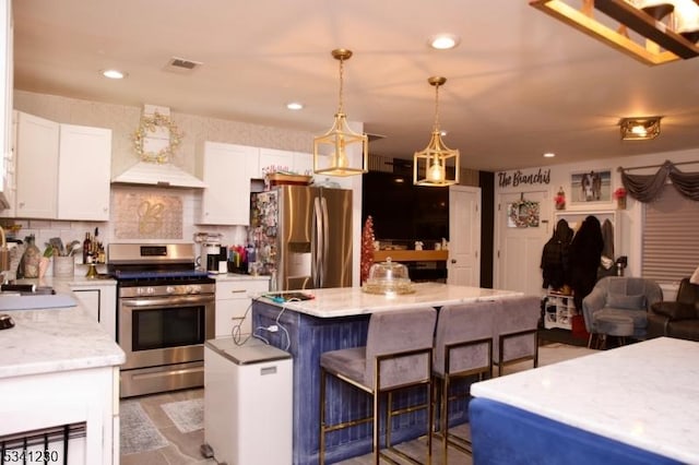 kitchen featuring visible vents, white cabinets, a kitchen island, stainless steel appliances, and a kitchen bar