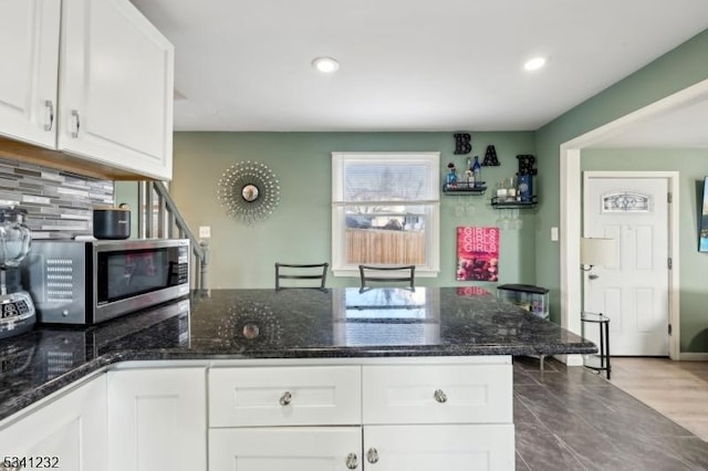 kitchen featuring tasteful backsplash, stainless steel microwave, white cabinets, dark stone countertops, and a peninsula