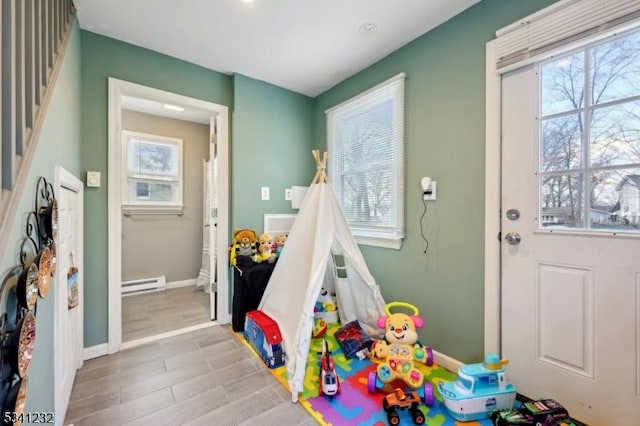 recreation room with a baseboard radiator, plenty of natural light, baseboards, and wood finished floors