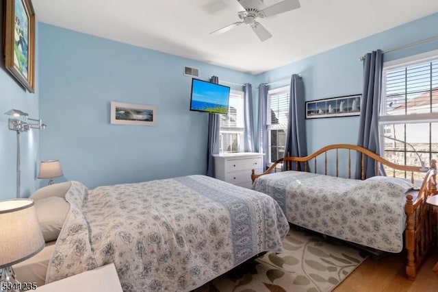 bedroom with ceiling fan, wood finished floors, and visible vents