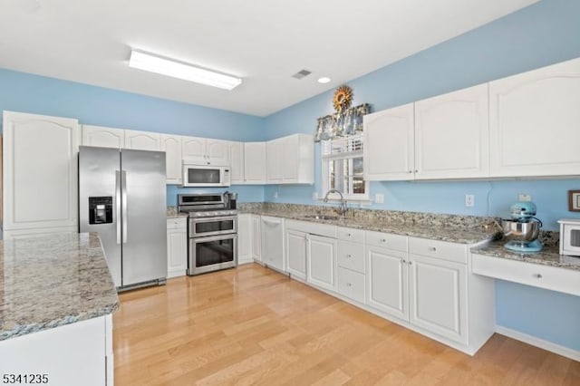 kitchen featuring stainless steel appliances, light wood-style flooring, white cabinetry, a sink, and light stone countertops