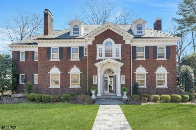 colonial inspired home featuring brick siding, a chimney, and a front lawn