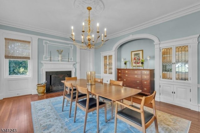 dining area featuring a brick fireplace, ornamental molding, wood finished floors, and a chandelier