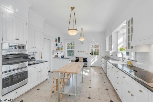 kitchen with stainless steel double oven, a sink, ornamental molding, glass insert cabinets, and white cabinetry