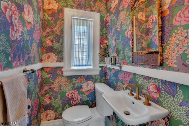 bathroom featuring a sink, toilet, and wallpapered walls