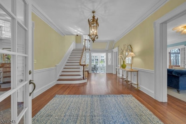 entryway featuring wood finished floors, stairway, an inviting chandelier, wainscoting, and crown molding