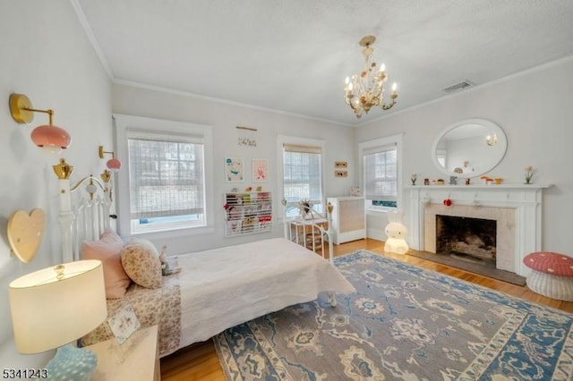 bedroom featuring wood finished floors, visible vents, a tiled fireplace, crown molding, and a notable chandelier