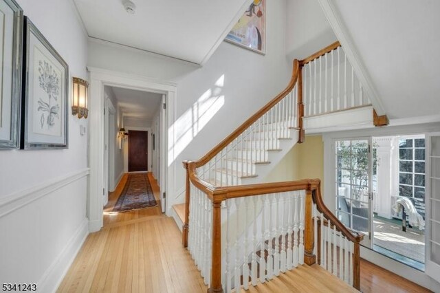 staircase with a high ceiling, a decorative wall, wood finished floors, and a wainscoted wall